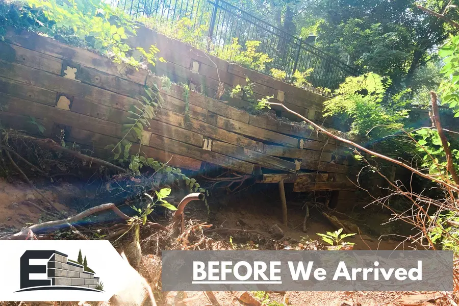 Before: rotting landscape timber retaining wall leaning and overgrown on a wooded slope